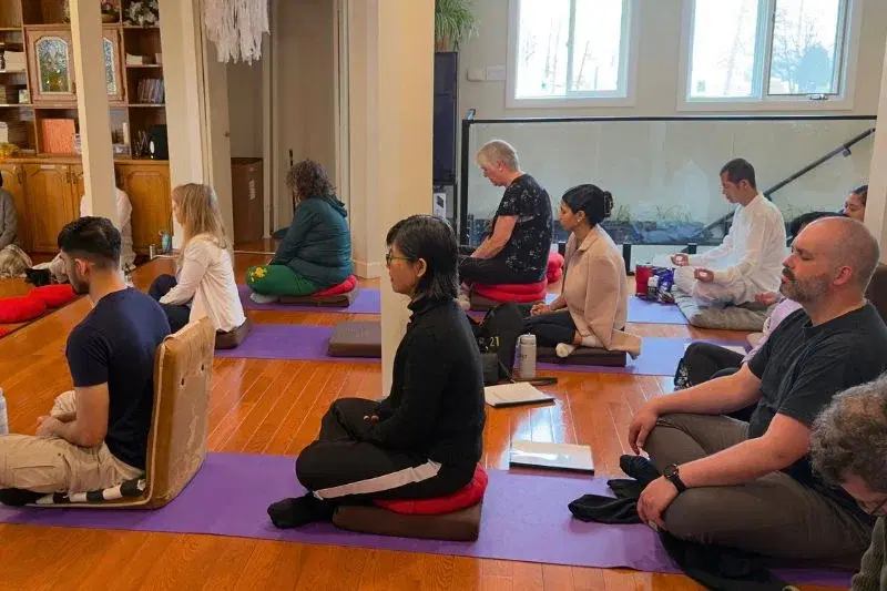 Diverse group of meditators seated on cushions practicing breathing meditation during a day-long retreat at Mahamevnawa Winnipeg